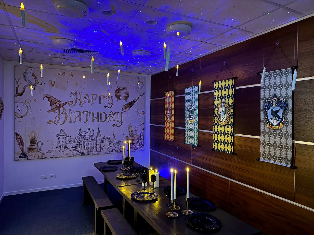 A wizard-themed birthday room with floating candle decorations, house-style banners and a long party table.