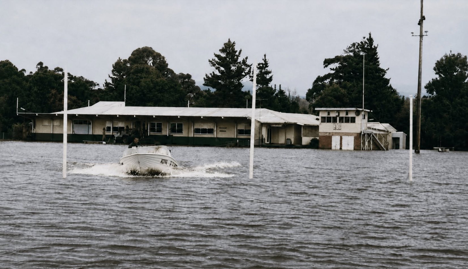 A motorboat crossing the flooded Yallourn Oval No. 1 in front of the oval’s club buildings.