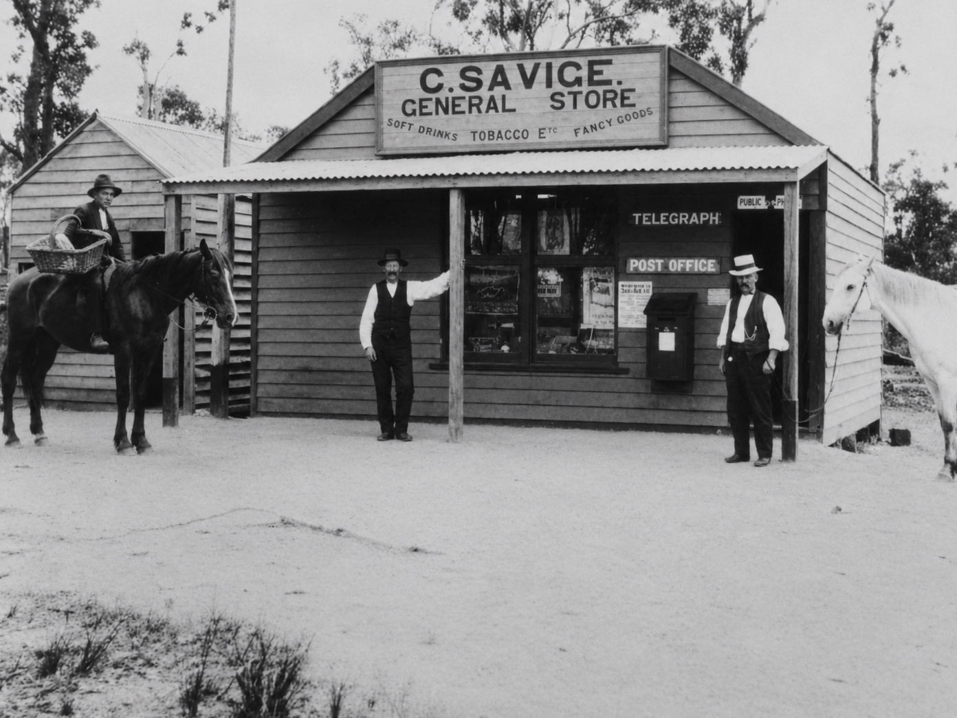 Restored black-and-white photograph of Charlie Savige’s general store, post office and telegraph office at Brown Coal Mine in 1917, with three men and two horses outside.
