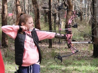 An archer taking aim at a 3D animal target in a bush setting, with colourful archery targets visible in the background.
