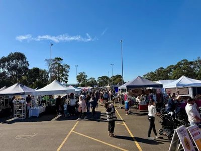 A busy outdoor market with stalls selling handmade crafts, plants and food, with families browsing in a relaxed community setting.