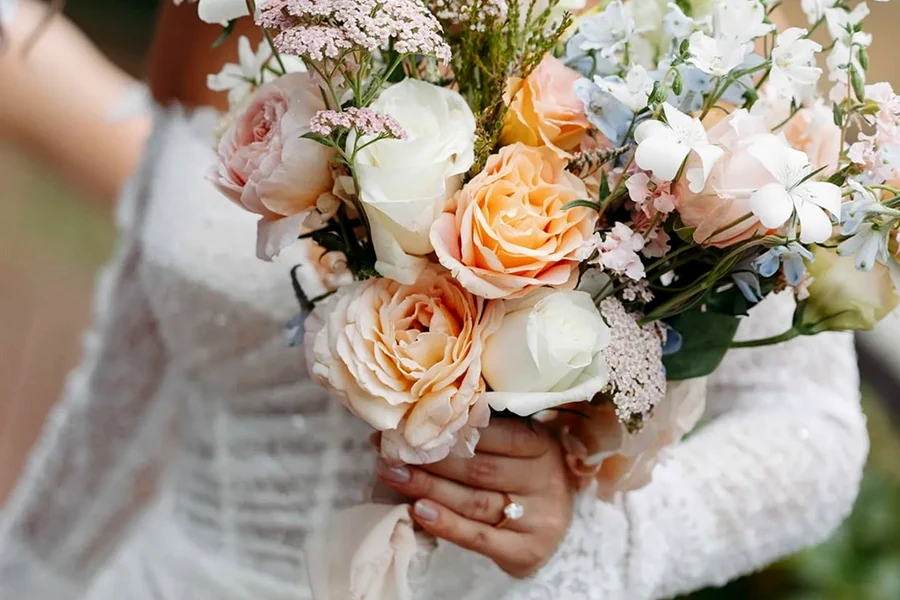 Two people in white holding pastel wedding bouquets.