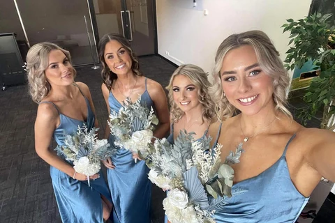Four people in blue dresses hold coordinated white, silver-green and blue dried bouquets.