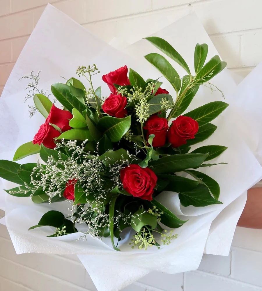 A bouquet of red roses and green foliage wrapped in white paper.