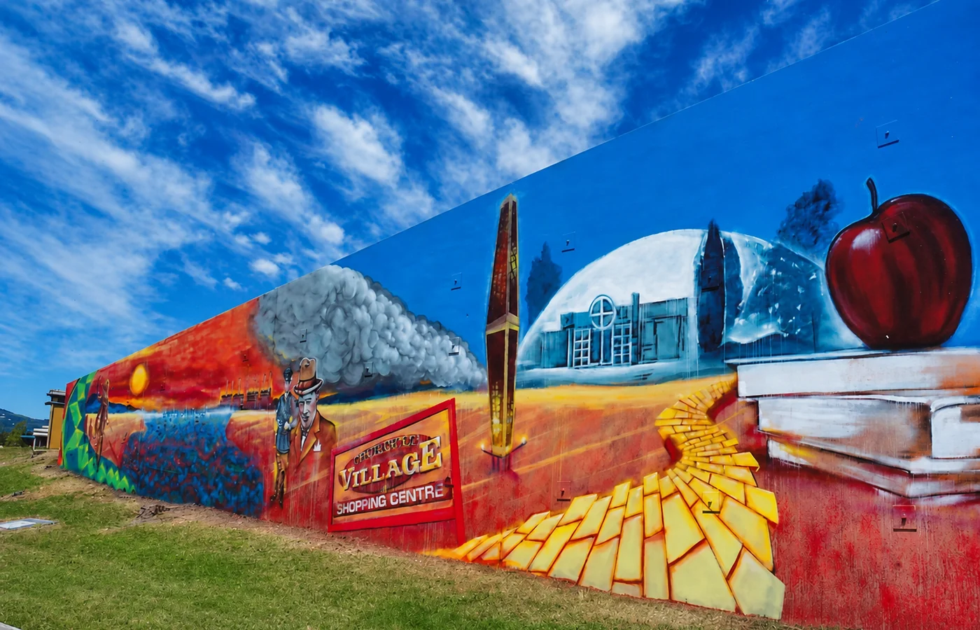 A long Churchill history mural showing the town symbol, a church, an apple and scenes of local industry beneath a vivid blue sky.