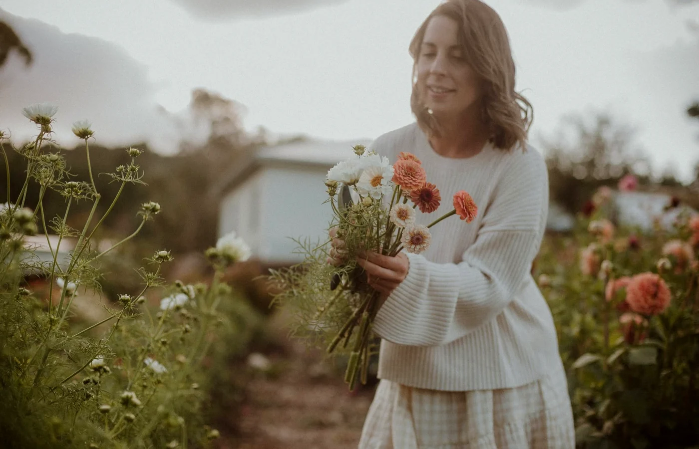 A woman holding freshly cut pink and white flowers among garden beds.