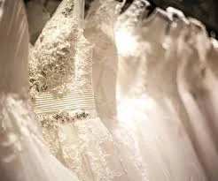 Close-up of white wedding dresses hanging together on a rail.