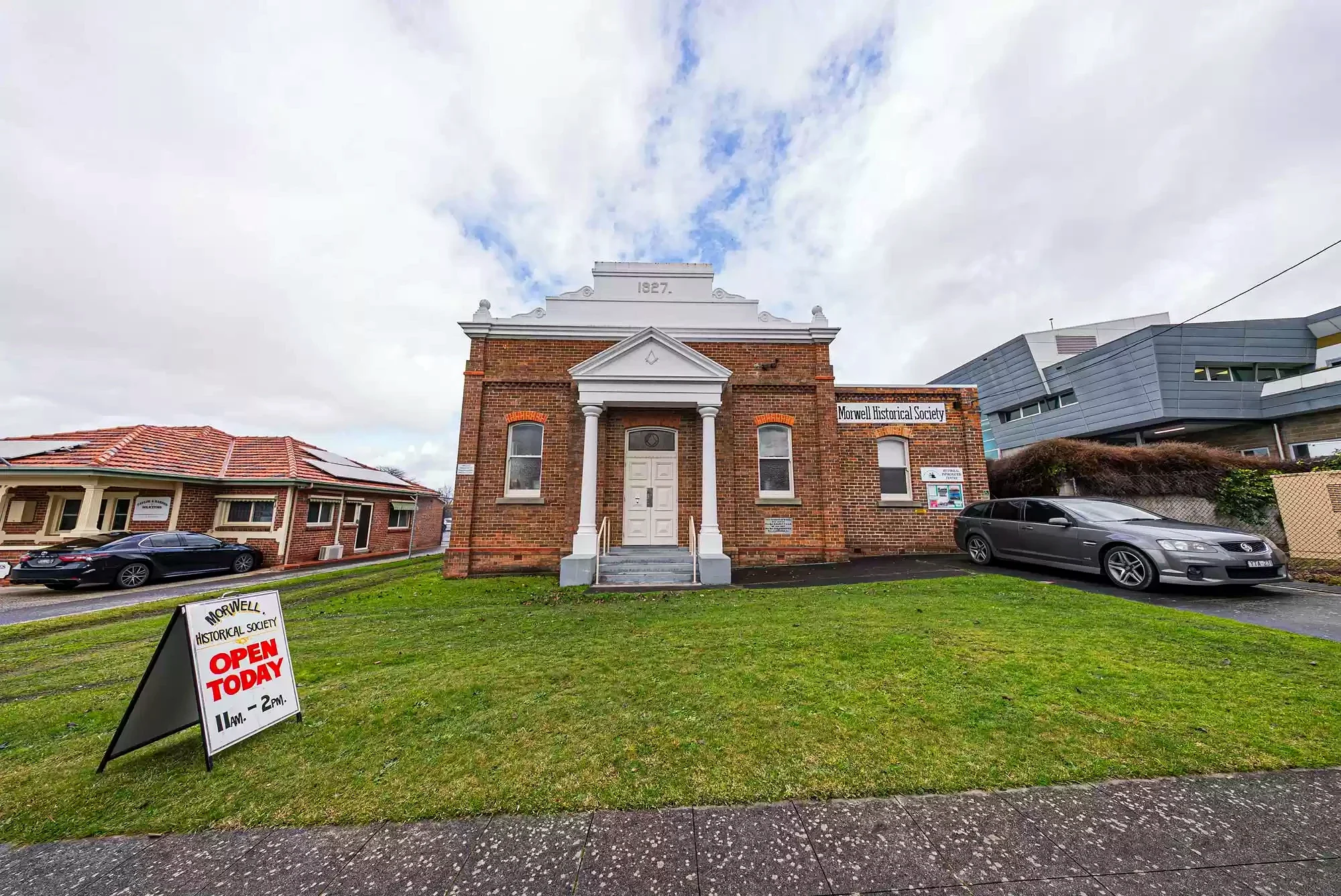 The brick Morwell Historical Society building beneath a cloudy sky, with an Open Today sign on the lawn.